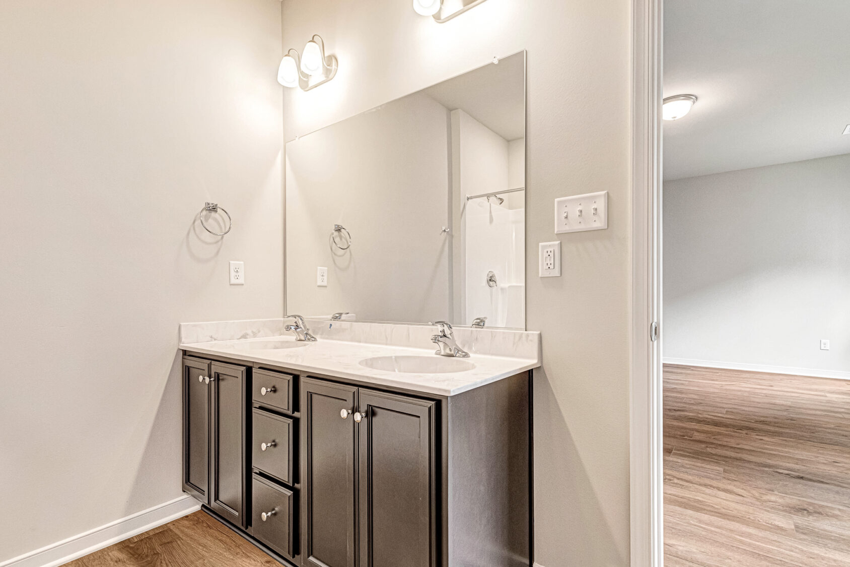 Modern bathroom in Lot 4, Somerset Hill, with double-sink vanity, large mirror, and wood flooring in the next room.