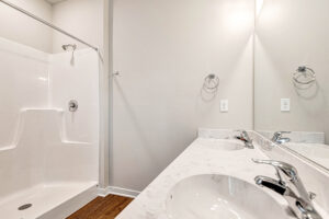 Somerset Hill Lot 4: White bathroom with double sink vanity, large mirror, and walk-in shower featuring a built-in seat.