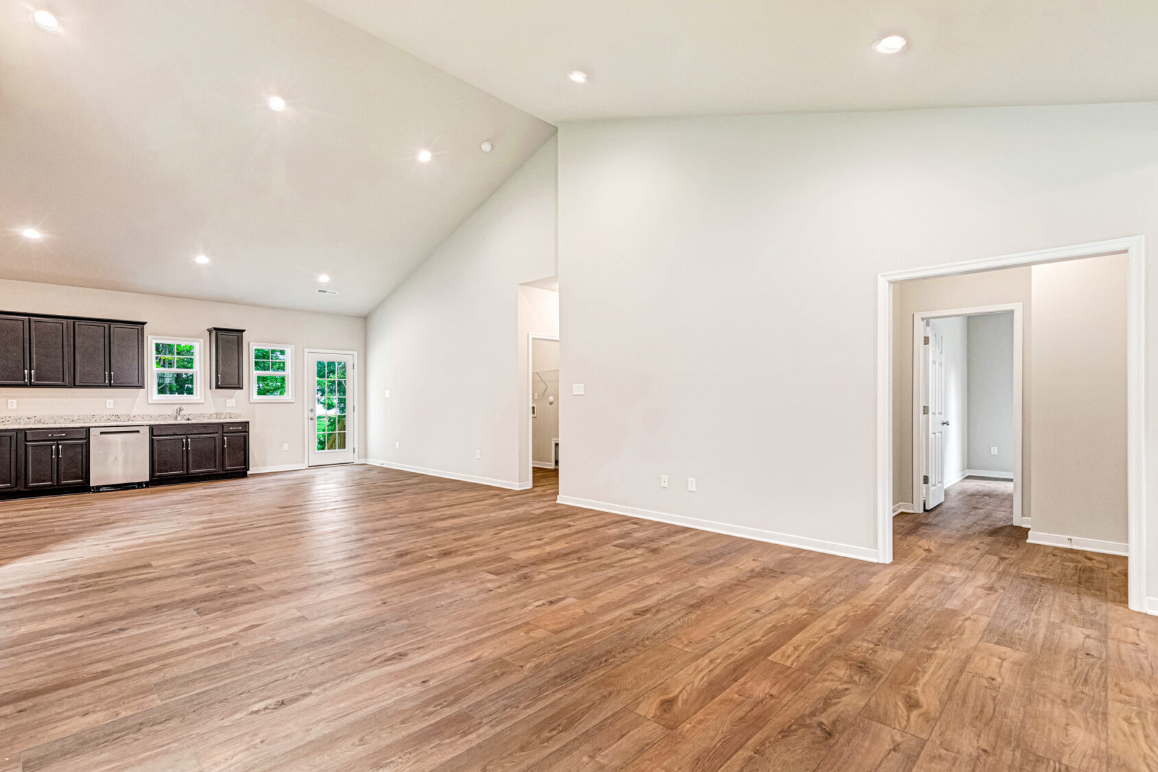 Spacious empty room in Somerset Hill with wood floors, white walls, and a modern kitchen with dark cabinets in the back.