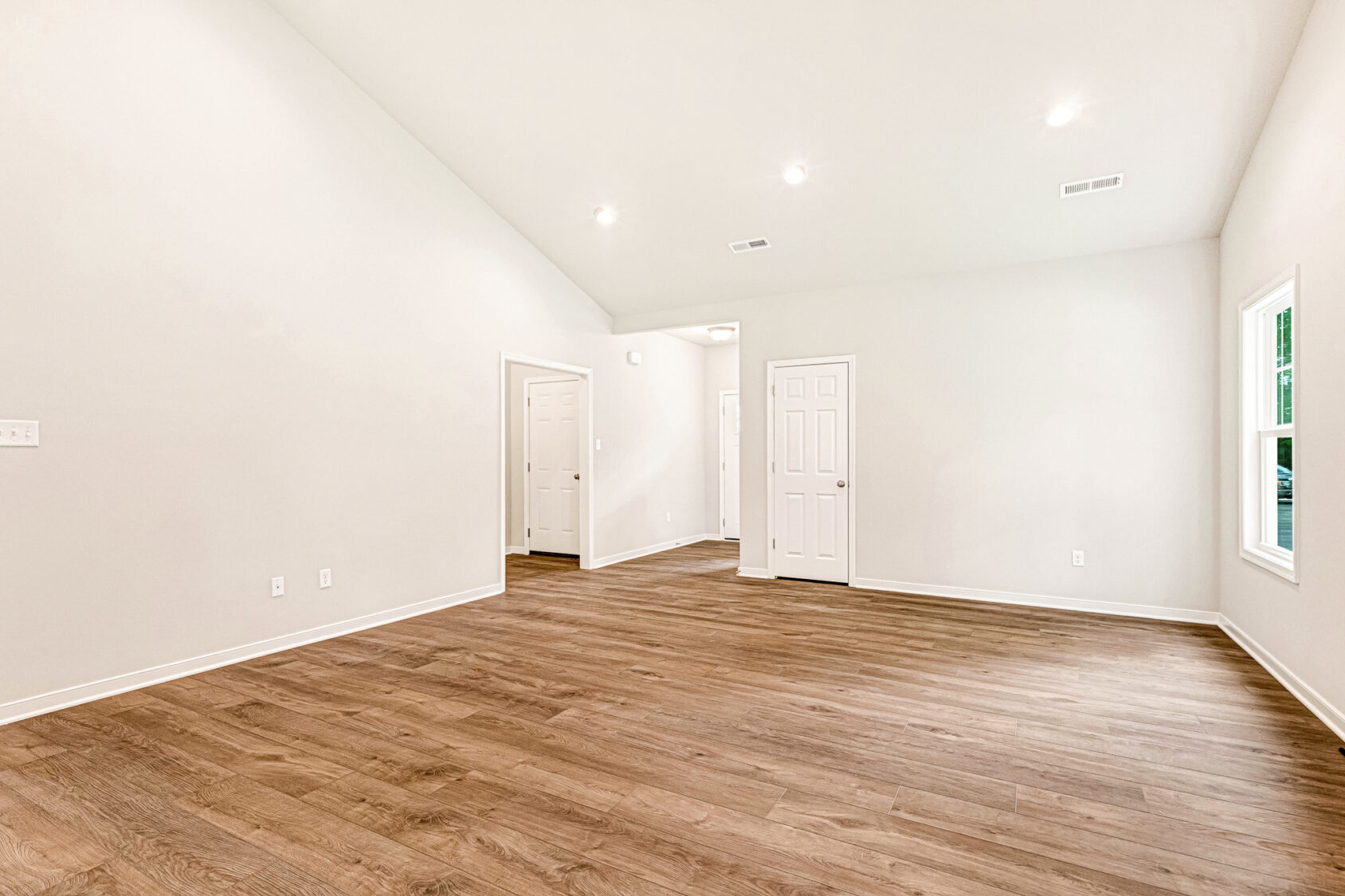 Bright empty room with wood floors, white walls, recessed lights, and multiple doors in Somerset Hill Lot 4.