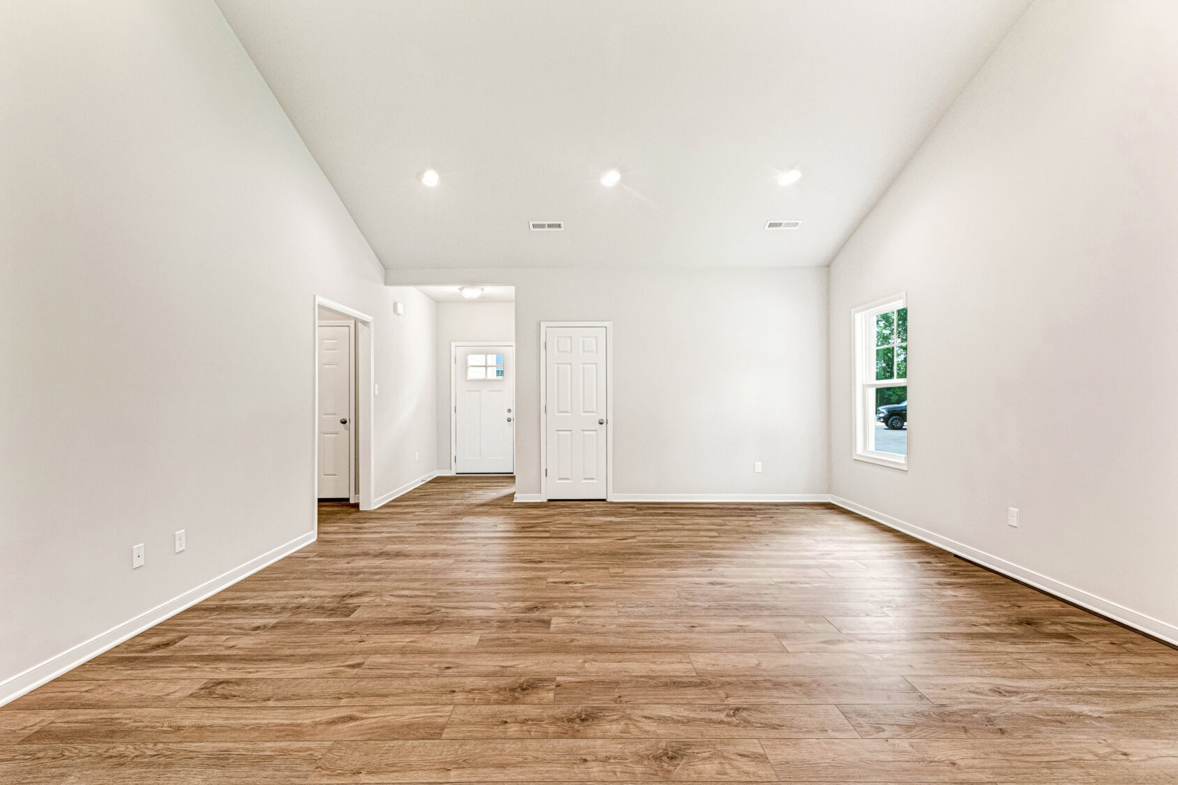Empty room in Somerset Hill's Lot 4 with wood flooring, white walls, recessed lights, a window, and three white doors.