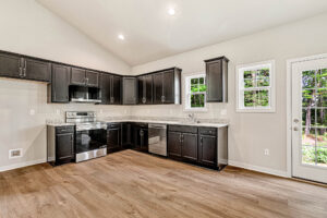 Modern kitchen with dark cabinets, stainless steel appliances, and wood floors in Somerset Hill Lot 4 overlooking greenery.