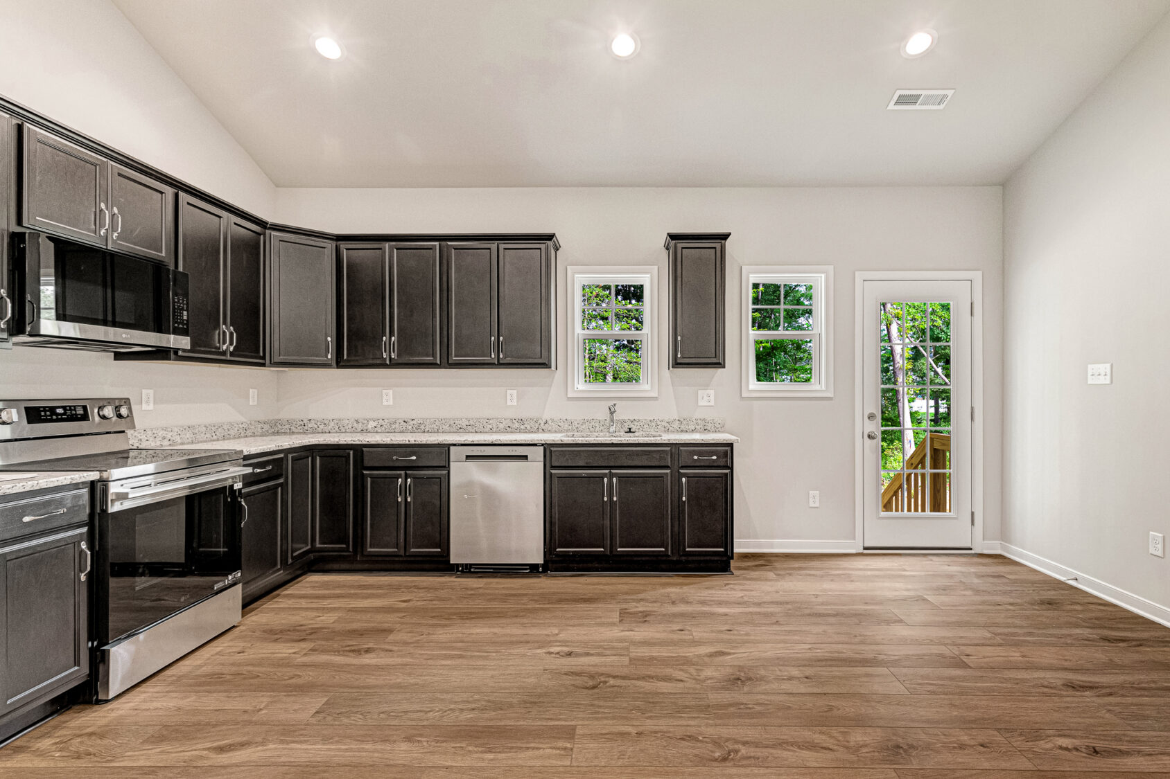 Modern kitchen in Somerset Hill, Lot 4 features dark cabinets, stainless appliances, light walls, and wood floors.