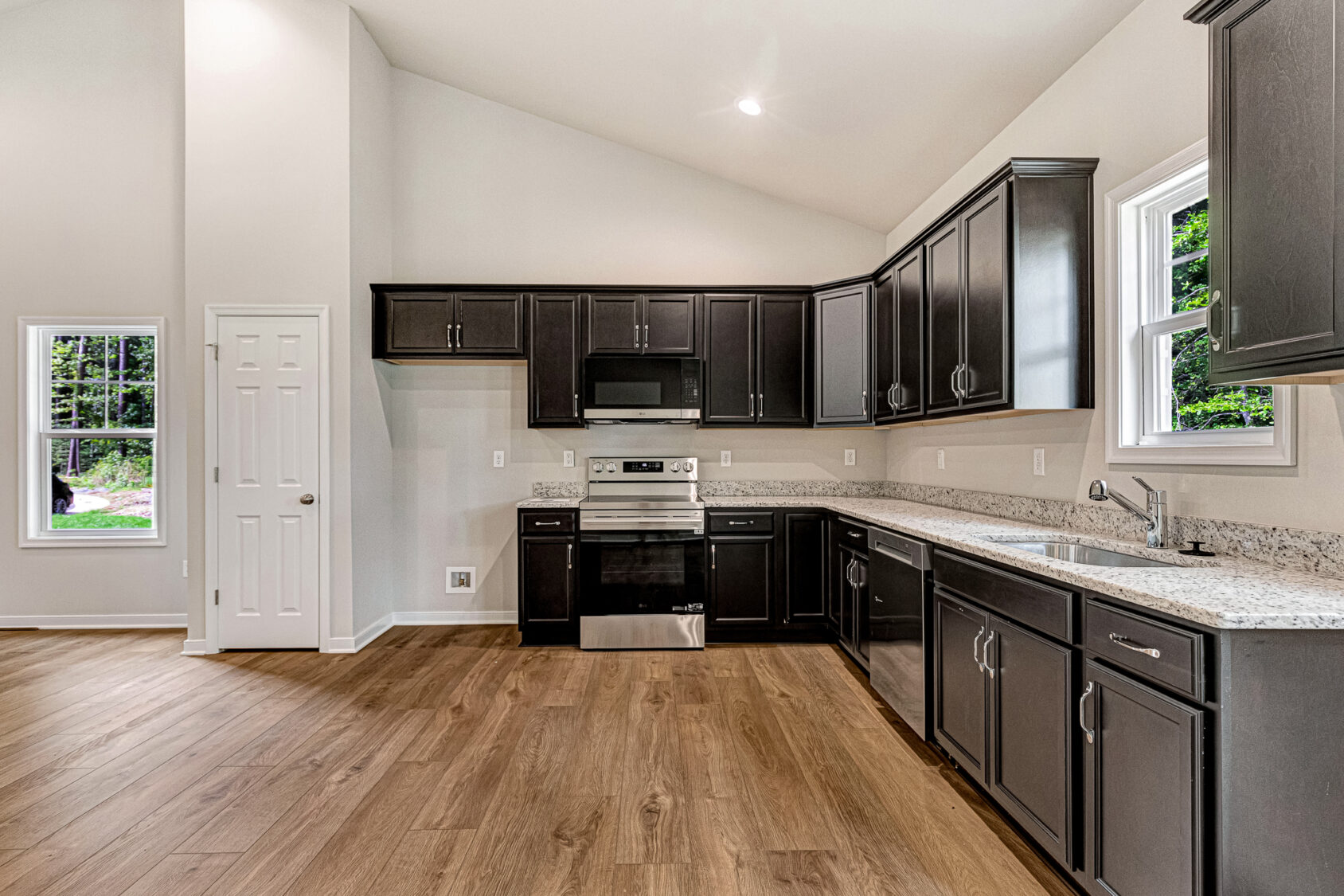 Modern kitchen in Somerset Hill with dark cabinets, stainless steel appliances, granite tops, and wood flooring.