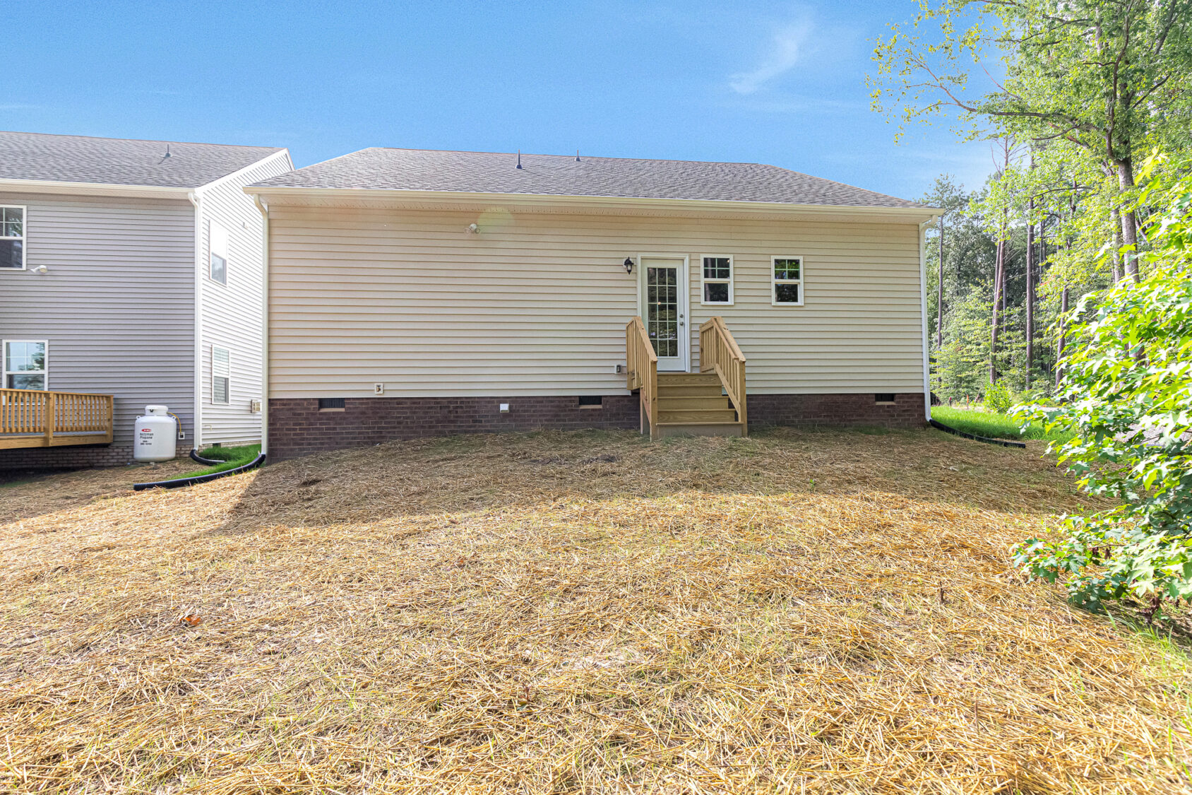 Back view of Somerset Hill Lot 4: beige house, small wooden steps, double doors, and a straw-covered yard.