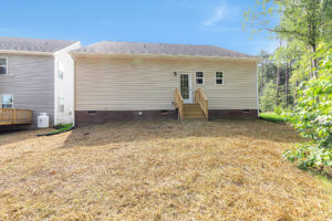 Back view of Somerset Hill Lot 4: beige house, small wooden steps, double doors, and a straw-covered yard.