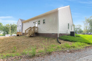 Lot 4, Somerset Hill: White single-story house with small wooden porch, brick foundation, and grassy yard under a blue sky.