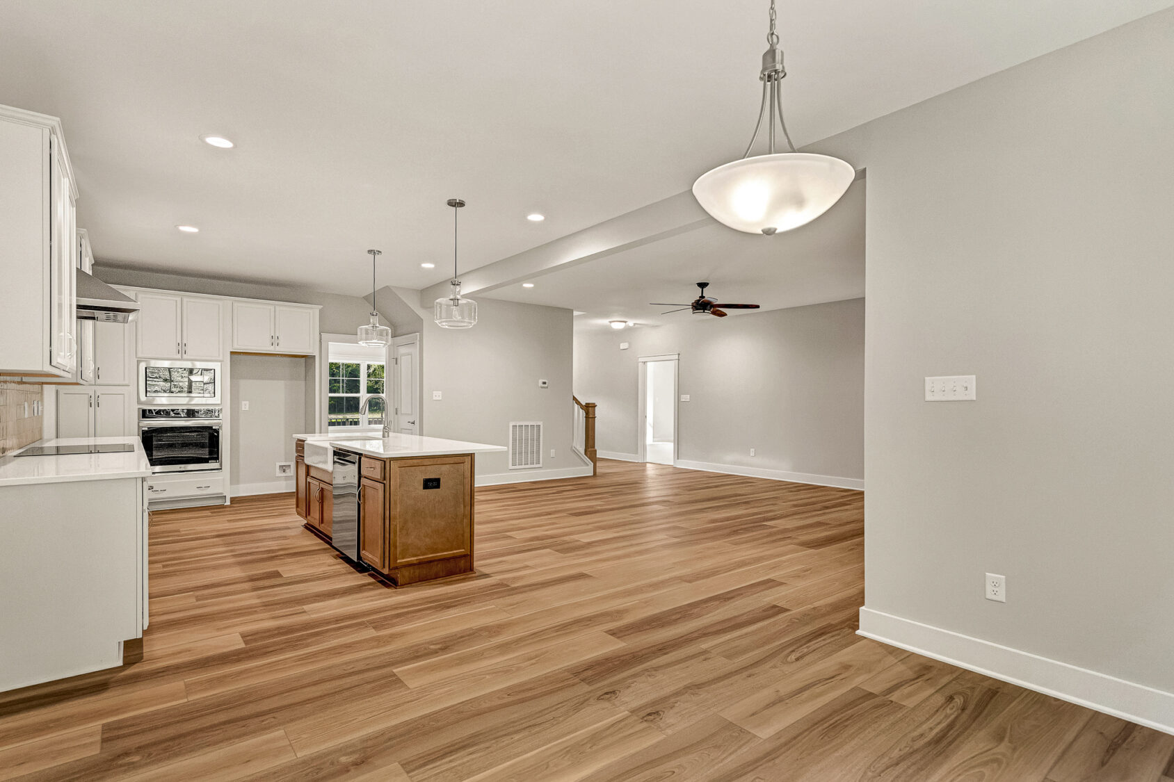 Modern open kitchen and living area in Somerset Hill Lot 7 with wood floors, white cabinets, island, and pendant lighting.