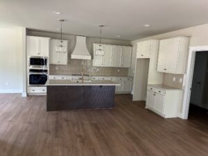 Modern kitchen in Lot 20 with white cabinets, island, wood floors, pendant lights, and built-in appliances.