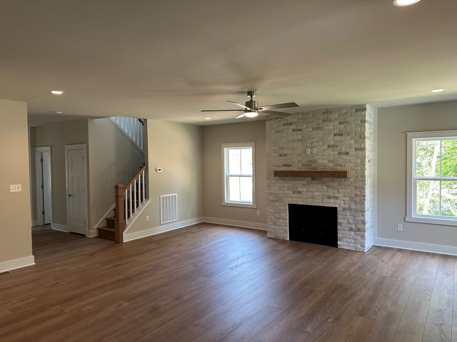 Spacious living room in Somerset Hill with wood floors, fireplace, ceiling fan, large windows, and stairs leading up.