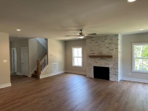 Spacious living room in Somerset Hill with wood floors, fireplace, ceiling fan, large windows, and stairs leading up.