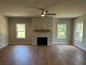 Bright Somerset Hill living room with wood floors, ceiling fan, and a brick fireplace between two sunny windows.