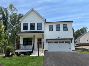 Modern two-story white house with black trim on Somerset Hill, Lot 20, features a porch and double garage under blue skies.