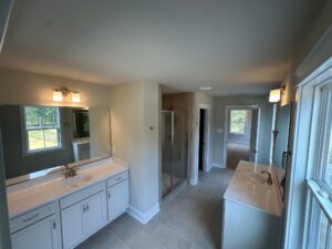 Somerset Hill Lot 20: Bathroom with double sinks, glass shower, large mirrors, and natural light on light tile floors.
