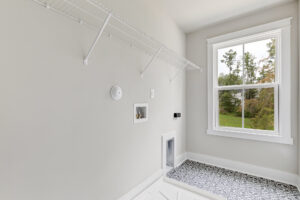 Lot 20 Somerset Hill: Empty laundry room with white wire shelf, patterned tile, window, and washer-dryer hookups.