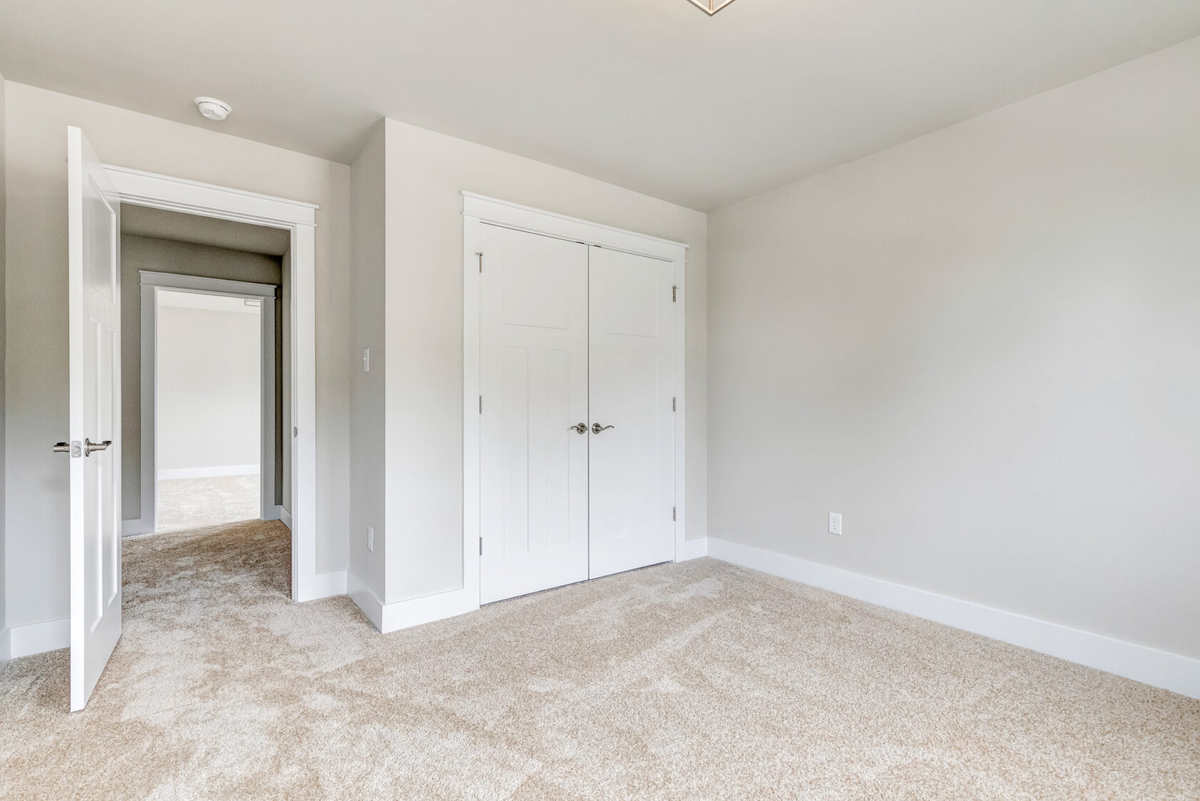Empty, bright Somerset Hill bedroom with beige carpet, white walls, double closets, and an open door to a hallway.