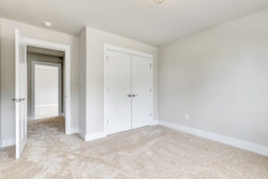 Empty, bright Somerset Hill bedroom with beige carpet, white walls, double closets, and an open door to a hallway.