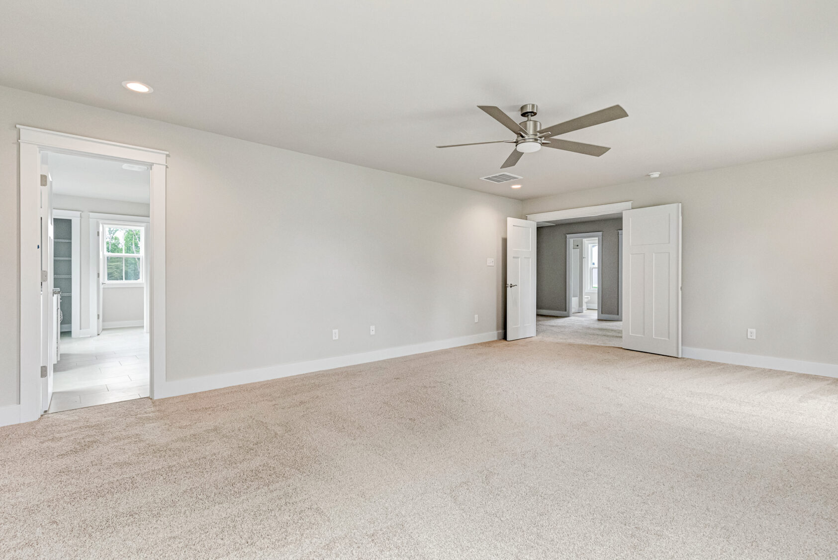 Spacious empty Somerset Hill bedroom with beige carpet, ceiling fan, and doors to other rooms.