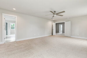 Spacious empty Somerset Hill bedroom with beige carpet, ceiling fan, and doors to other rooms.