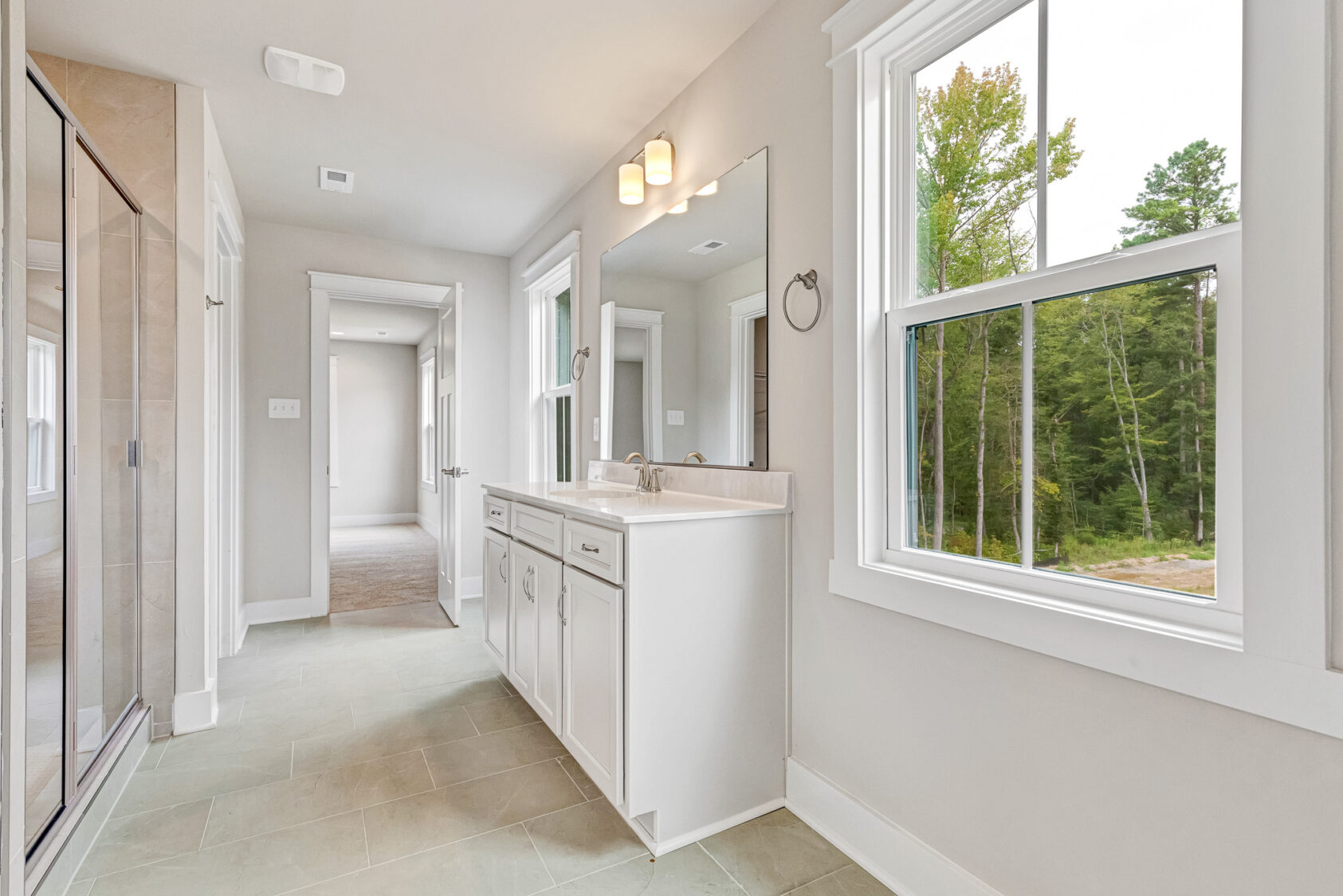 Bright Somerset Hill bathroom with double-sink vanity, large window, glass shower, and beige tile floor.