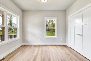 Bright empty room with light wood flooring, white walls, and large windows in Somerset Hill Lot 20.