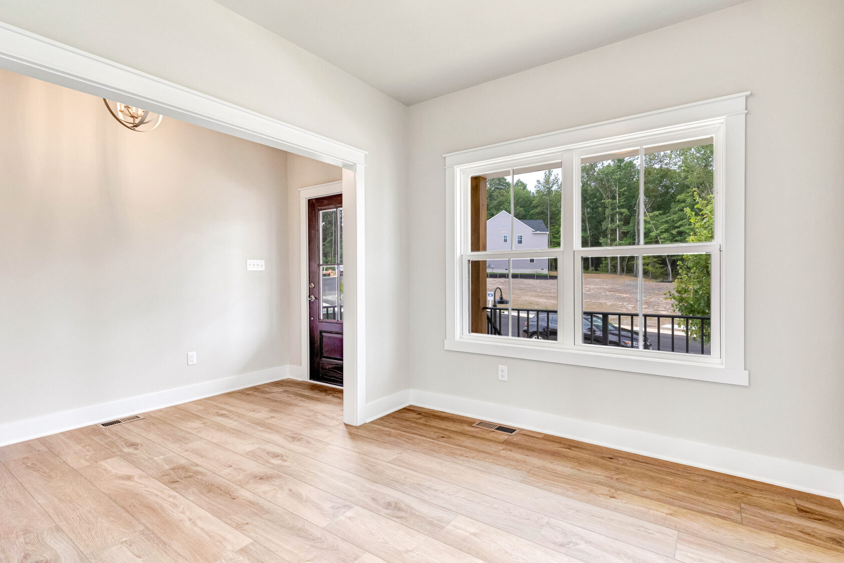 Bright empty room with light wood floors in Somerset Hill, large window, white trim, and glass door leading outside.