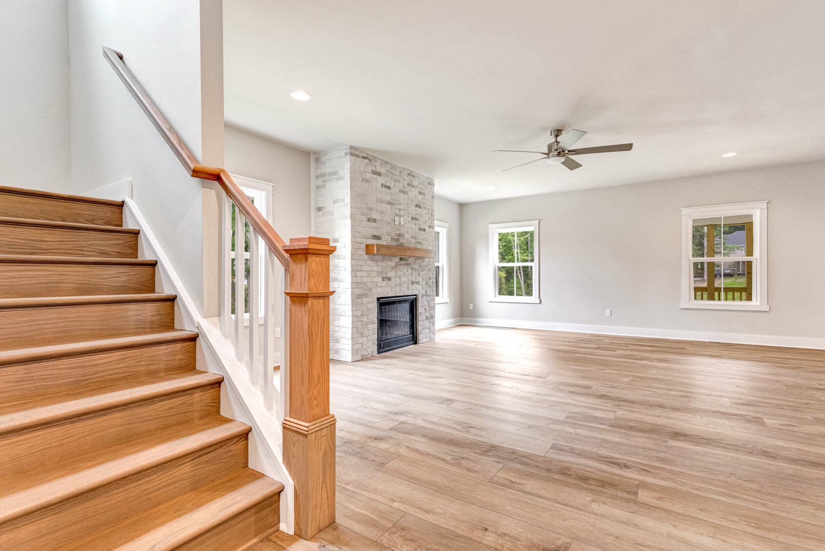 Bright living room with wood floors, fireplace, large windows, and wooden staircase on Lot 20 in Somerset Hill.