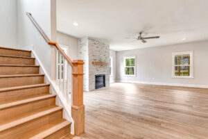 Bright living room with wood floors, fireplace, large windows, and wooden staircase on Lot 20 in Somerset Hill.