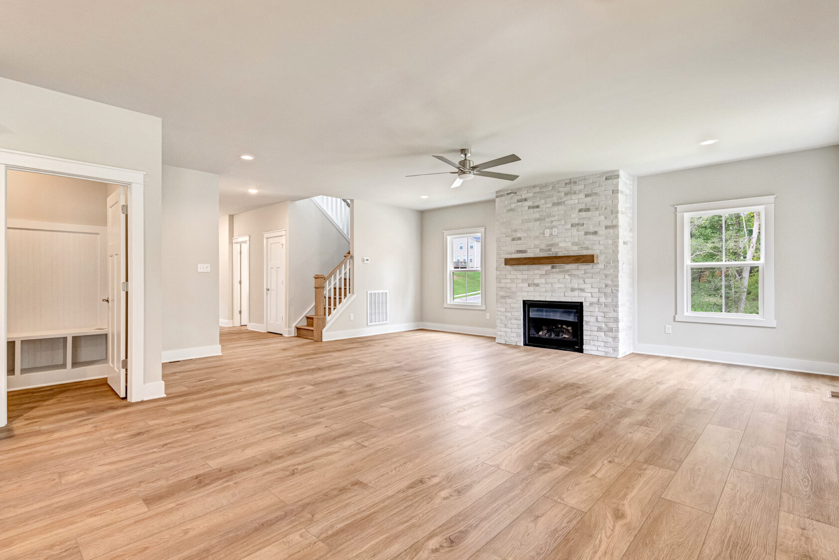 Bright living room in Somerset Hill with wood floors, white walls, fireplace, large windows, and ceiling fan.