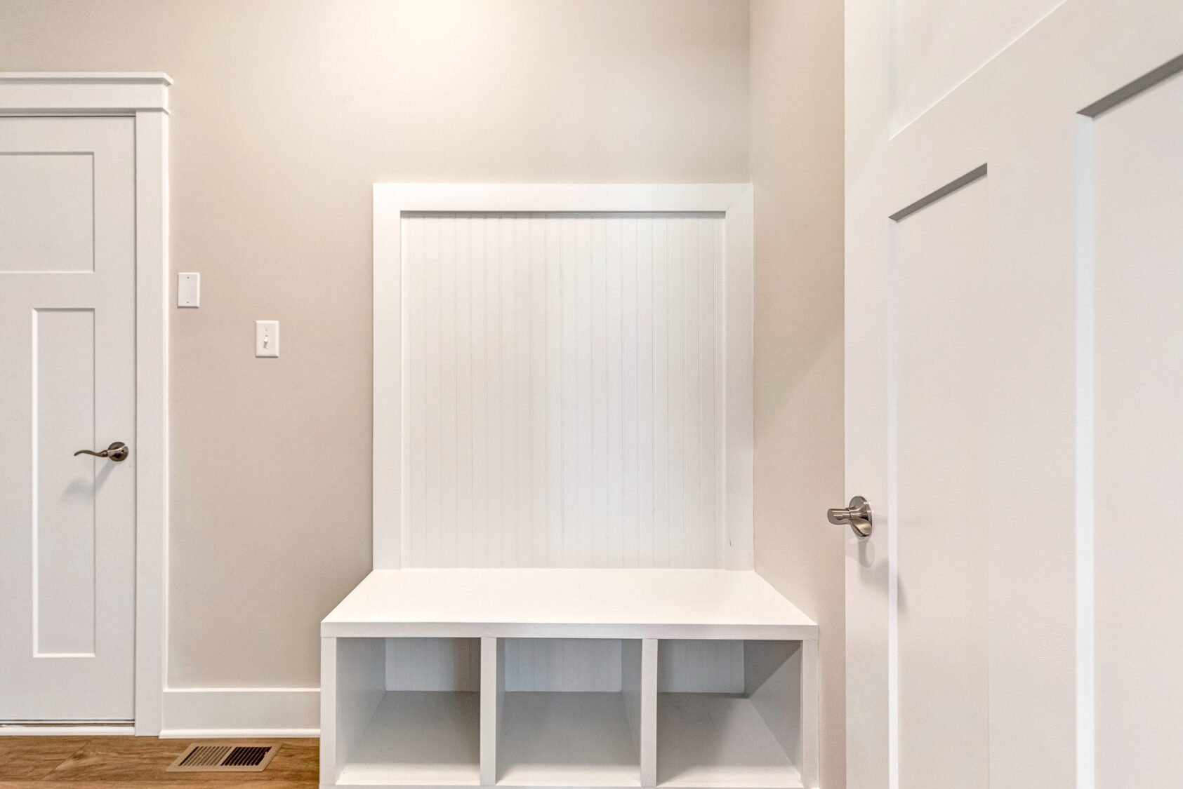 White built-in bench with cubby storage in the entryway of Lot 20, Somerset Hill, next to closed doors.