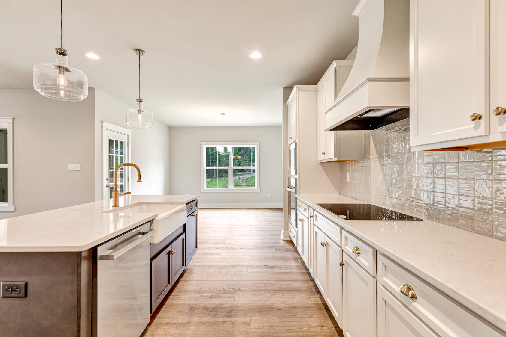 Modern kitchen in Lot 20, Somerset Hill with white cabinets, pendant lights, and a large window overlooking the yard.