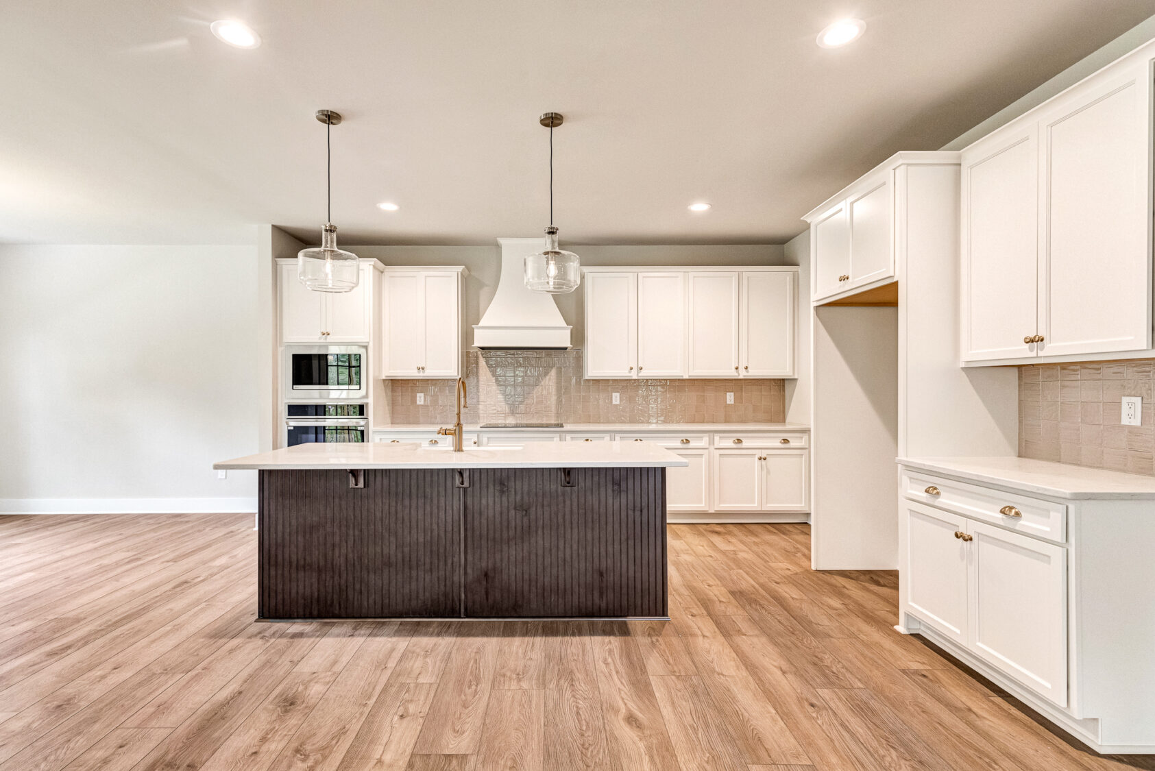 Modern Somerset Hill kitchen with white cabinets, dark island, pendant lights, wood floors, and neutral backsplash.