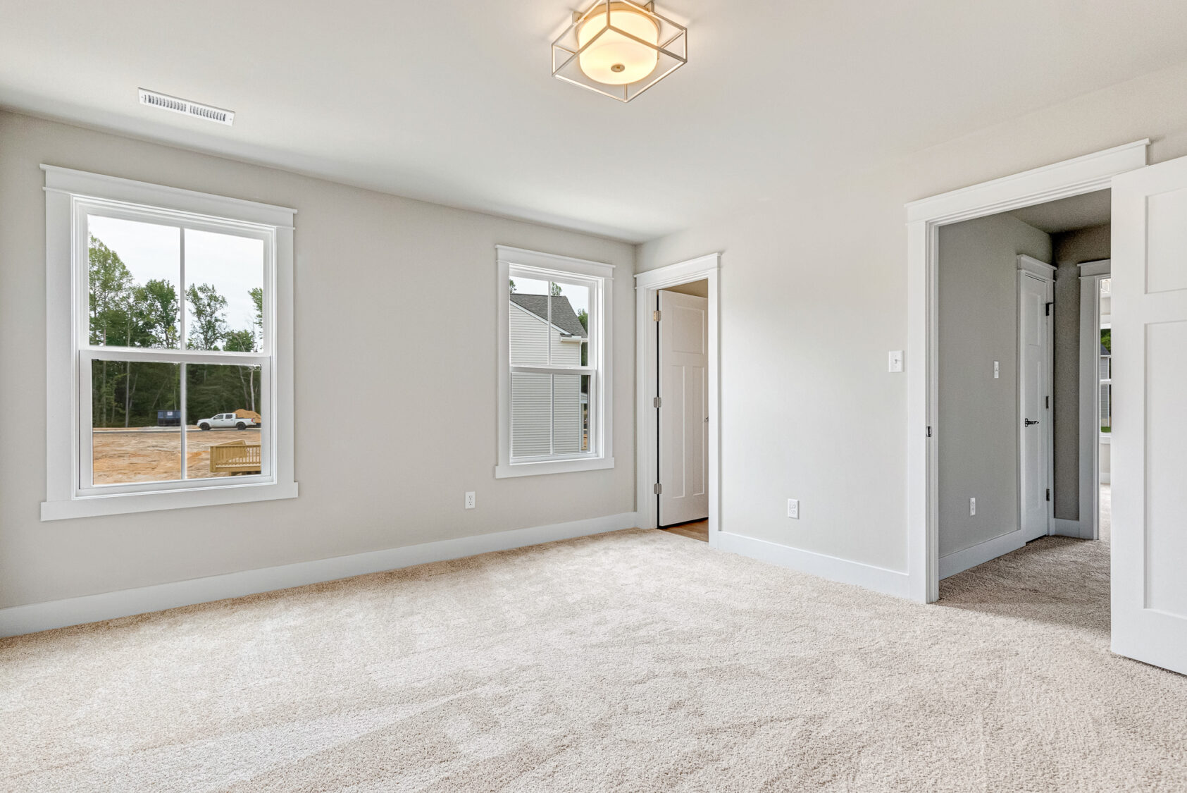 Bright empty Somerset Hill bedroom with beige carpet, two windows, a closet, and white walls.