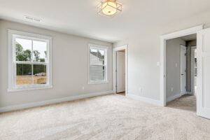 Bright empty Somerset Hill bedroom with beige carpet, two windows, a closet, and white walls.