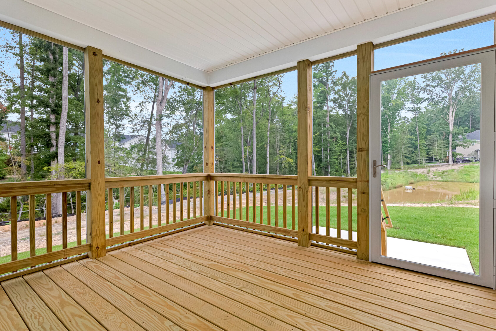 Screened-in wooden porch at Somerset Hill, with railing, open door, and views of trees and grassy Lot 20 outside.