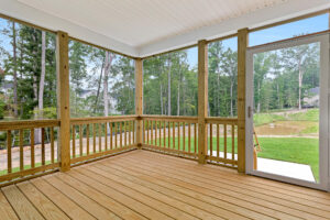 Screened-in wooden porch at Somerset Hill, with railing, open door, and views of trees and grassy Lot 20 outside.