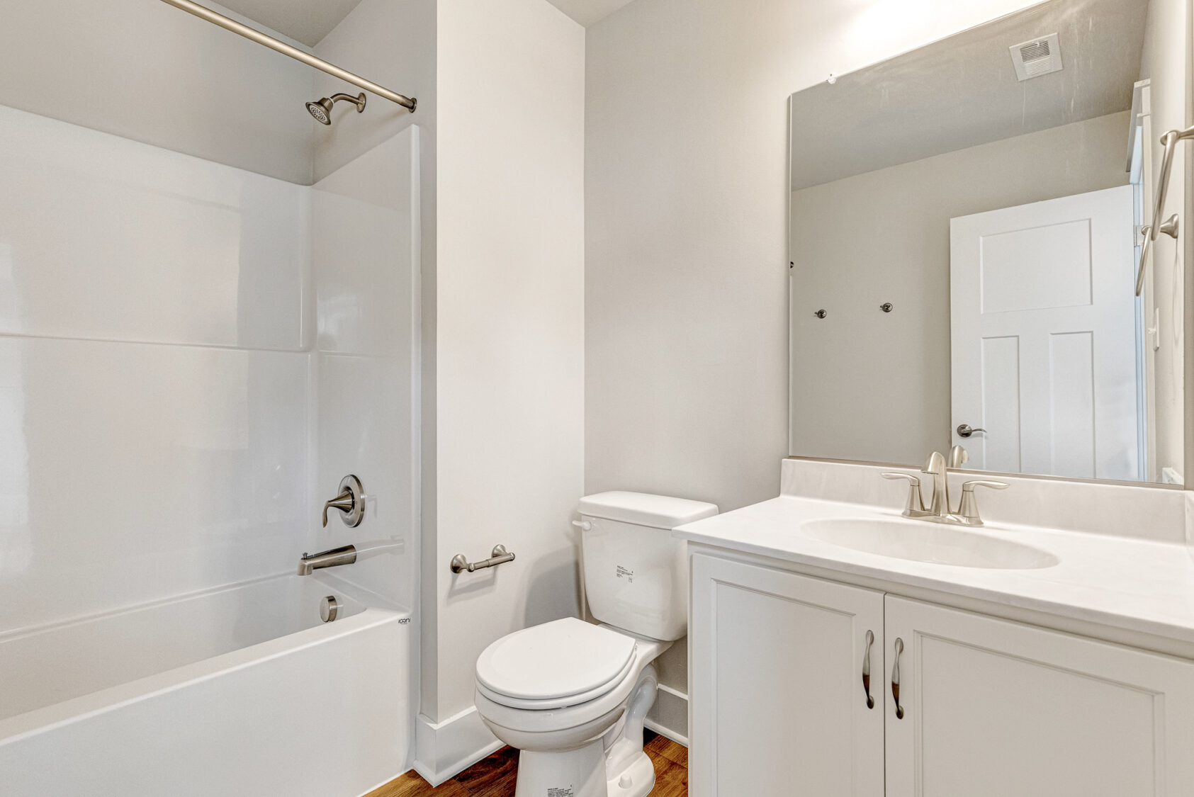 Somerset Hill Lot 20: White bathroom with a tub, toilet, sink, and large mirror above the vanity with simple fixtures.