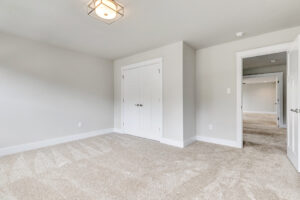 Empty beige carpeted bedroom on Lot 20, Somerset Hill, features double-door closet, white walls, and open hallway door.