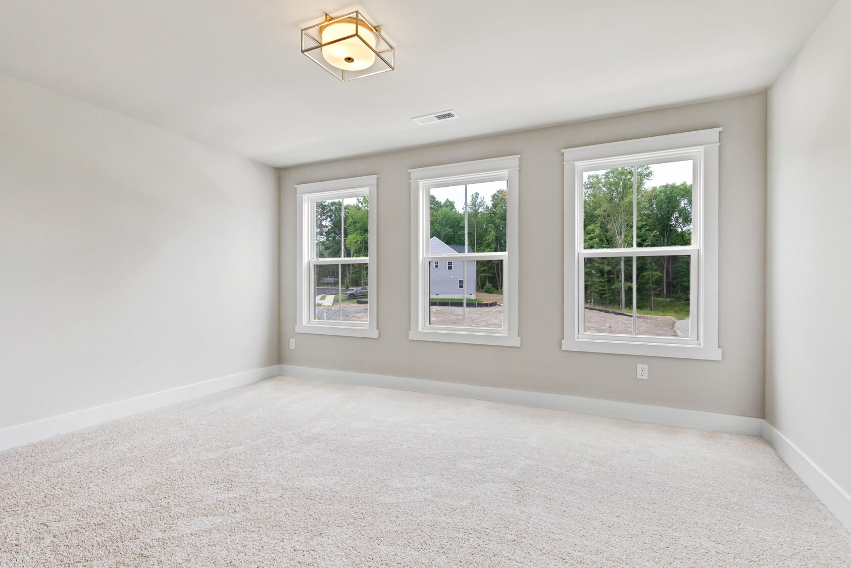 Bright empty room in Somerset Hill with three large windows, beige carpet, and a modern ceiling light fixture.